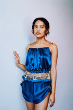 Load image into Gallery viewer, Long shot of a woman wearing a blue silk camisole and tap pants. She has her hand on the wall and looks straight at the camera.