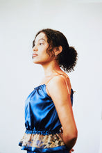 Load image into Gallery viewer, A woman stands side on wearing a deep blue gathered silk camisole trimmed with a gold lace hip frill.