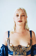 Load image into Gallery viewer, A front view of a woman in the Anna 1/4 cup bralette. The bra cup edge sits at around nipple level. The front is decorated with a hand made blue and gold rose and hand sewn pearls. The straps are made from wide blue silk. The front panel and the cups are layered with gold lace.