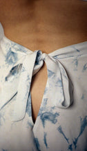 Load image into Gallery viewer, A close up of the bow that fastens the bamboo indigo tap pants. It extends out of the waistband and leaves a triangular opening beneath it showing some of the lower back. The image shows the beautiful variation in tone in the patches of indigo dye against the off white base fabric.