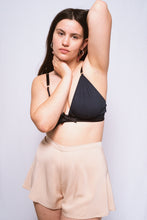 Load image into Gallery viewer, An image of a woman, shot from the front wearing the Cacao bamboo silk tap pants with the Artemis bralette. The tap pants are a pale latte shade and catch the light gently. They sit on the waist with a 1 inch waistband and fall from the hips in gentle folds to the top of the thigh.