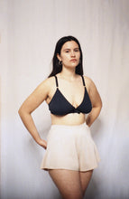 Load image into Gallery viewer, A woman with long brown hair stands looking at the camera with her hands behind her back. She wears the Artemis bamboo bralette and cacao bamboo tap pants. They flare out from the waistband over her hips to the top of her thighs.