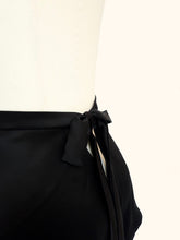 Load image into Gallery viewer, A close up on the bow fastening on the Emmeline black silk tap pants shot on a stand from the side. The 1 inch waistband is visible as well as the V shaped back.