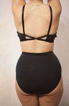 Load image into Gallery viewer, A shot of the back of a woman with her arms in the air. The image shows the back of the artemis bralette and high waist knickers. The back of the knickers is a single piece of jersey and the waistband is in a contrasting black.