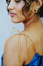Charger l&#39;image dans la galerie, close up on the shoulder of a woman wearing a blue silk camisole. The strap is doubled thin gold ribbon, it ties in a bow at the shoulder.
