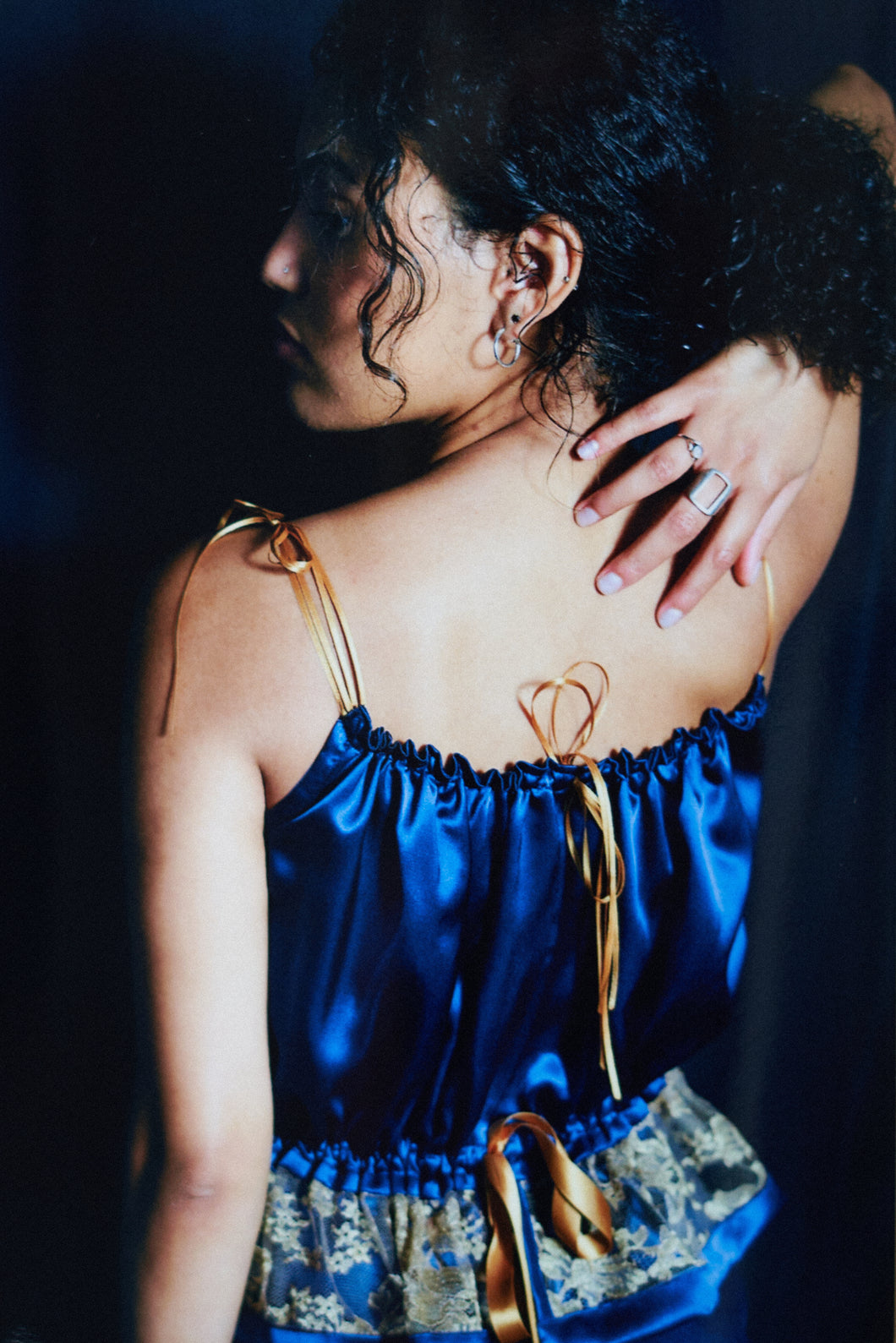 back view of a woman wearing a gathered blue silk camisole it ties with gold ribbons at the neck and waist