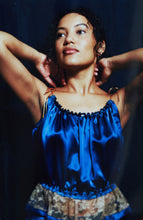Load image into Gallery viewer, front view of a woman weather a gathered blue silk camisole there are 4 pearls at the centre of the neckline. She holds her hands behind her neck.
