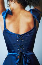 Load image into Gallery viewer, A back view of a woman in the Anna stays. the silk is deep blue the back scoops down and laces up with a black cotton corset lace. The eyelets are brass.
