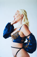Load image into Gallery viewer, A side view of a woman in the Anna 1/4 cup bralette. the side of the bra is blue silk and ends half way round the body, transitioning into a multiple strap back. The back elastics are black with gold rings and sliders.
