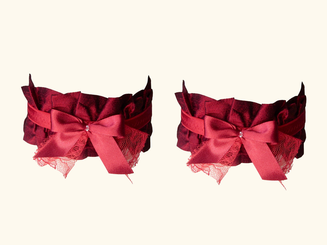 Front view of a pair of dark red garters. They are decorated iwth red bows with tiny glass beads in the centre.