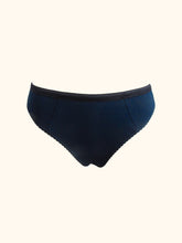 Charger l&#39;image dans la galerie, The front of the Artemis bamboo thong on a stand. The front is constructed from petrol blue bamboo jersey and has 2 vertical seams, around 1/3 from the side seams. It also has a contrasting black waistband. There is no other decoration.
