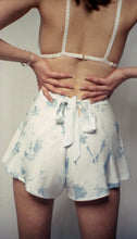 Cargar imagen en el visor de la galería, An image of a woman wearing the bamboo silk indigo tap pants, shot from the back. The tap pants fasten with a bow at the centre back and there is a small triangular opening below it. The indigo dye is scattered across the fabric at random, creating an abstract feel. Her hands are on her hips. She also wears the Lily bralette with silk covered straps.
