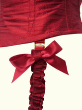 Load image into Gallery viewer, A close up of the bows on the suspender straps, the centre is made of the same silk as the body. The straps are detachable, held in place by gold G hooks. The top half of the straps is encased in ruffled red silk.
