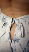 Cargar imagen en el visor de la galería, A close up of the bow that fastens the bamboo indigo tap pants. It extends out of the waistband and leaves a triangular opening beneath it showing some of the lower back. The image shows the beautiful variation in tone in the patches of indigo dye against the off white base fabric.

