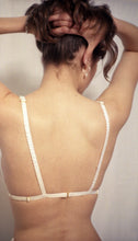 Charger l&#39;image dans la galerie, A model holds her hair up to show the back of the Lily bralette. The straps are covered in gathered ivory silk, and are adjustable at the shoulders and sides. The shoulder straps are sewn into the band strap. The back fastens with a gold G hook.
