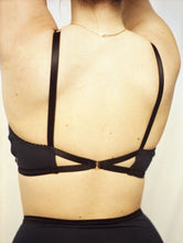 Load image into Gallery viewer, A close up of the back of the Artemis bralette. The back fastens with a small gold hook, with two pieces of black elastic leading to it, causing a triangle shape on either side leading into the band. The straps go up from the edge of the band.
