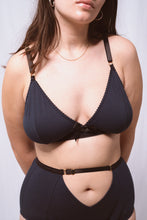 Charger l&#39;image dans la galerie, A close up of a woman&#39;s torso from the front wearing the Artemis bralette and high waist knickers. Both are in petrol blue bamboo jersey with black elastics and gold hardware. The front of the knickers has a cross over panel detail that creates an upside down triangle at the waistline around the belly button. The waistband is adjustable above the triangle and has a gold slider.

