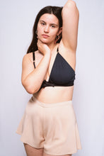 Cargar imagen en el visor de la galería, An image of a woman, shot from the front wearing the Cacao bamboo silk tap pants with the Artemis bralette. The tap pants are a pale latte shade and catch the light gently. They sit on the waist with a 1 inch waistband and fall from the hips in gentle folds to the top of the thigh.
