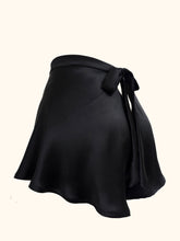 Cargar imagen en el visor de la galería, The side back view of the black silk Emmeline tap pants shot on a stand. The back fastens with a bow that extends from the waistband and is around 1 inch wide. There is a small triangular gap below the bow that would expose the lower back. The fabric is bias cut and flows down over the hips to the top of the thigh. The fabric is generously cut and folds gently as it falls.
