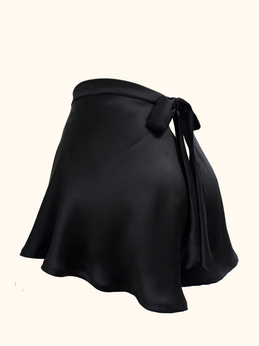 The side back view of the black silk Emmeline tap pants shot on a stand. The back fastens with a bow that extends from the waistband and is around 1 inch wide. There is a small triangular gap below the bow that would expose the lower back. The fabric is bias cut and flows down over the hips to the top of the thigh. The fabric is generously cut and folds gently as it falls.