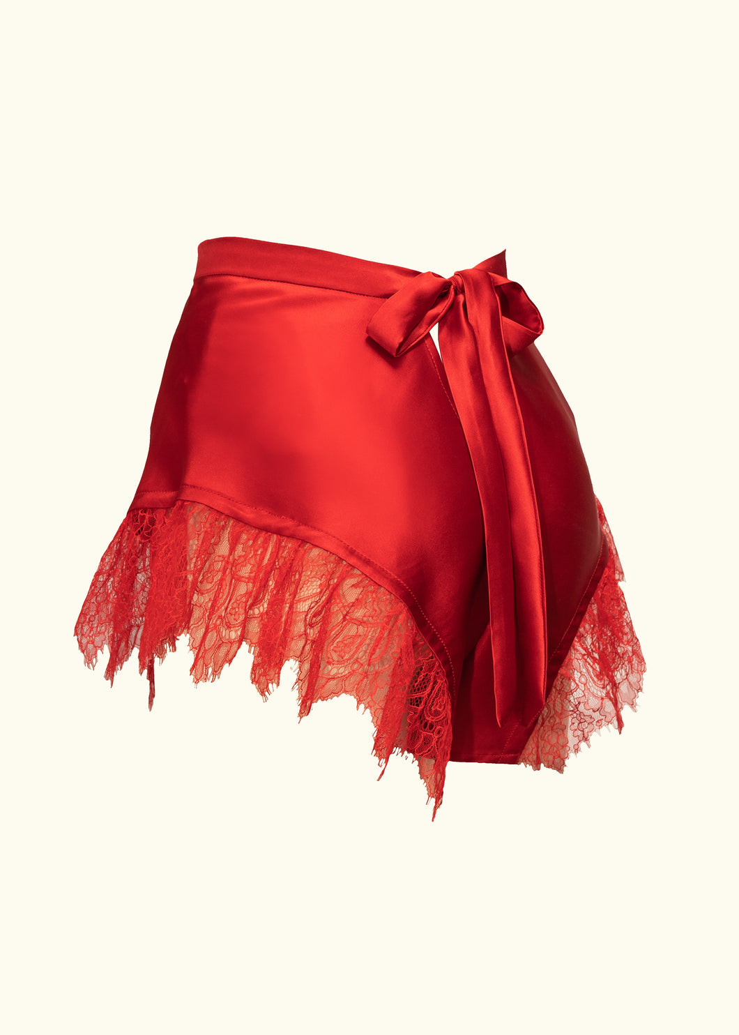 A side back view of the Olenska tap pants. The leg has a curved seam that loops up from the centre front and back down to the centre back, this hem line is trimmed with a deep french lace frill. The tap pants are a mid red.
