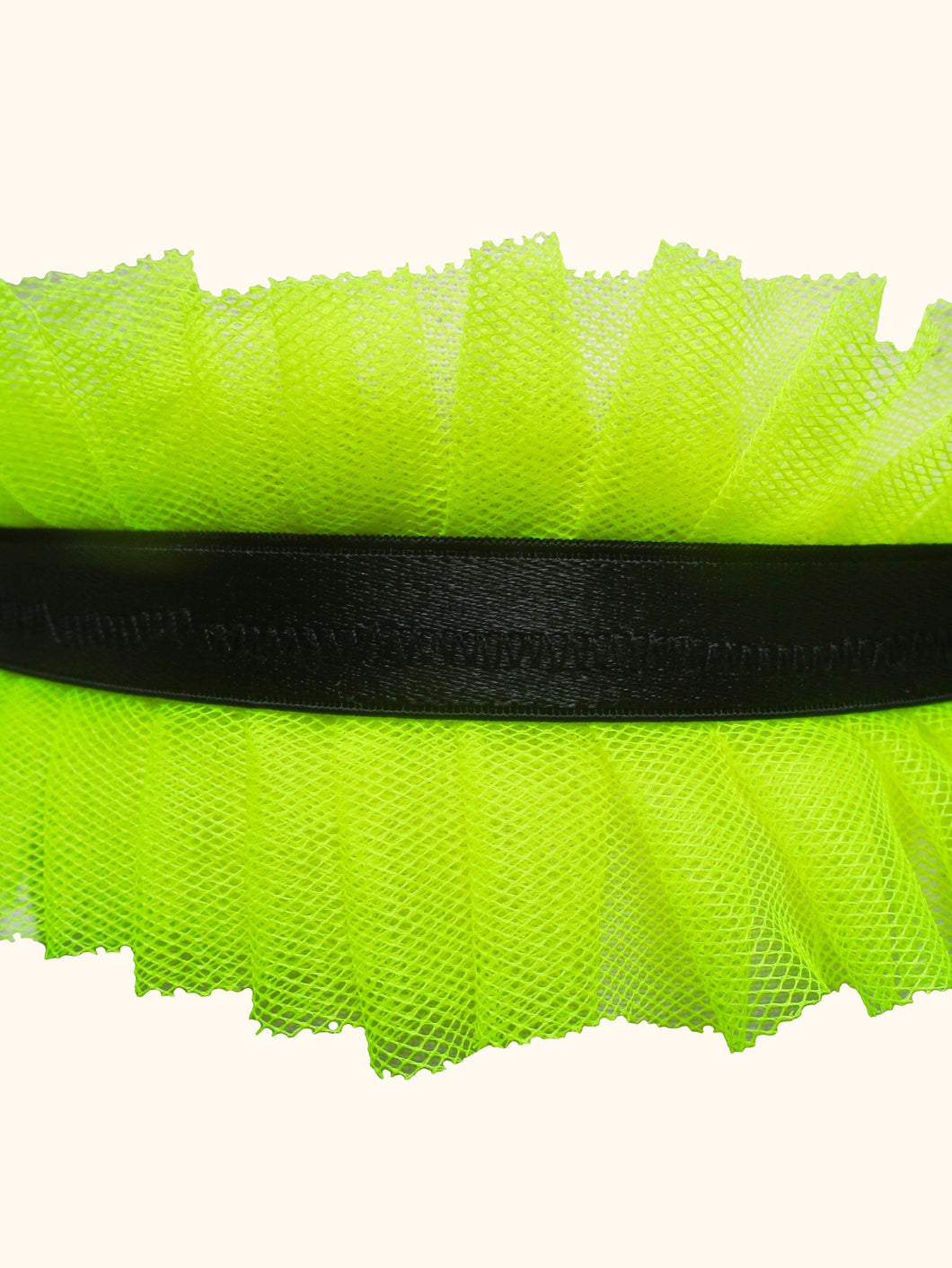 A close up of a garter with a central black satin elastic band. Either side of the band are neon yellow pleated tulle frills.